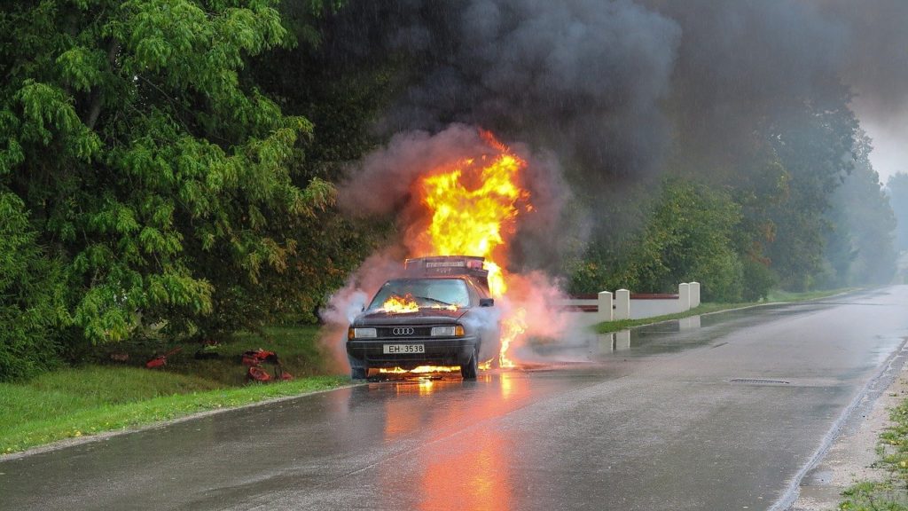 A car on fire in the middle of a road.