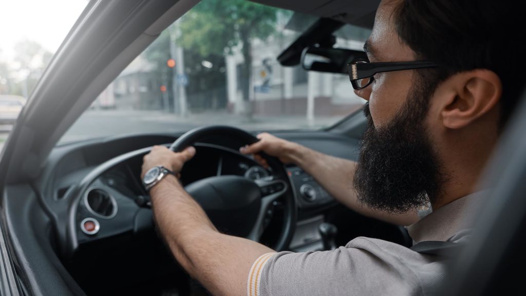 A man with glasses is driving in the street